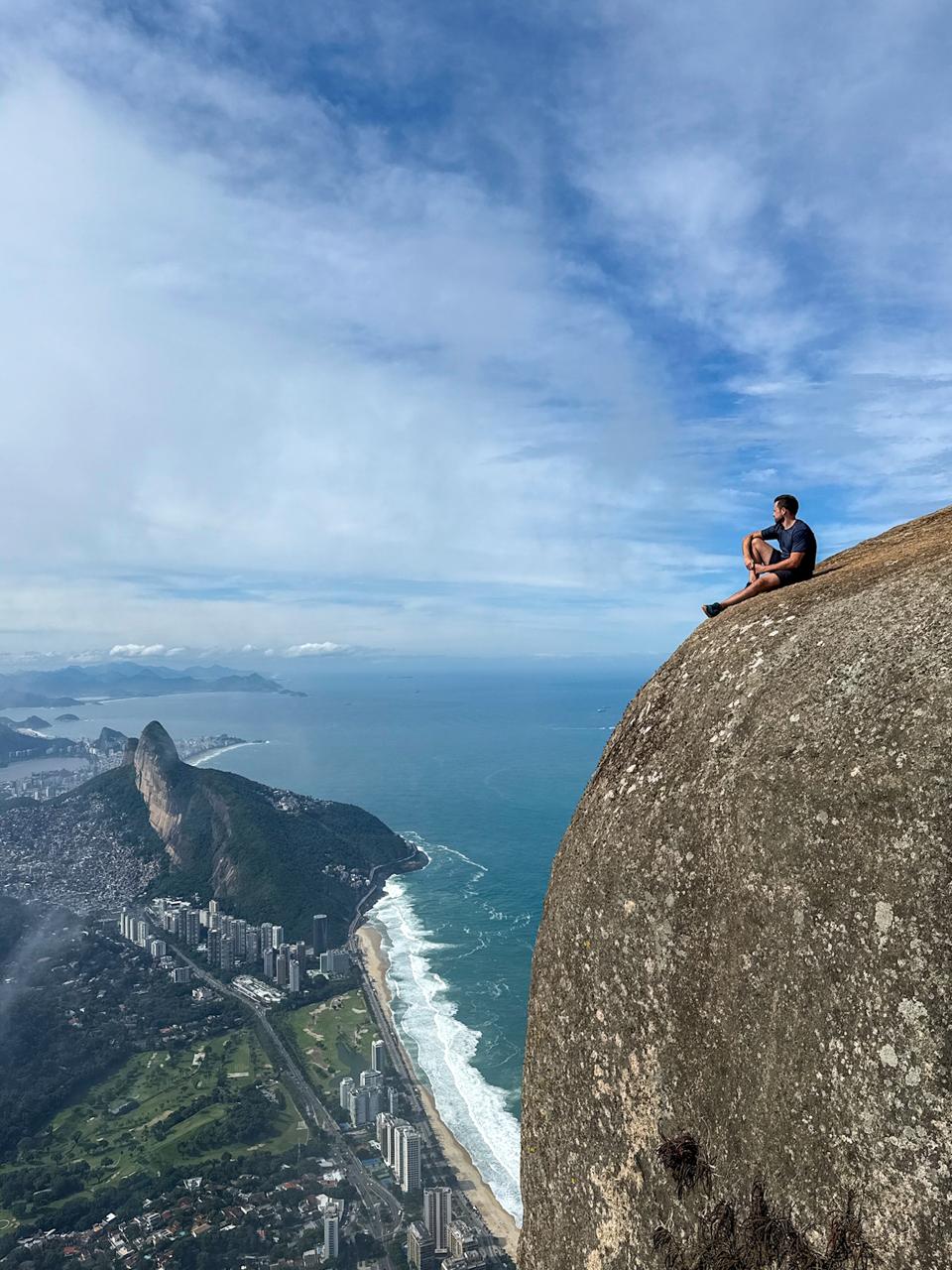 Pessoa sentada no penhasco da Pedra da Gávea